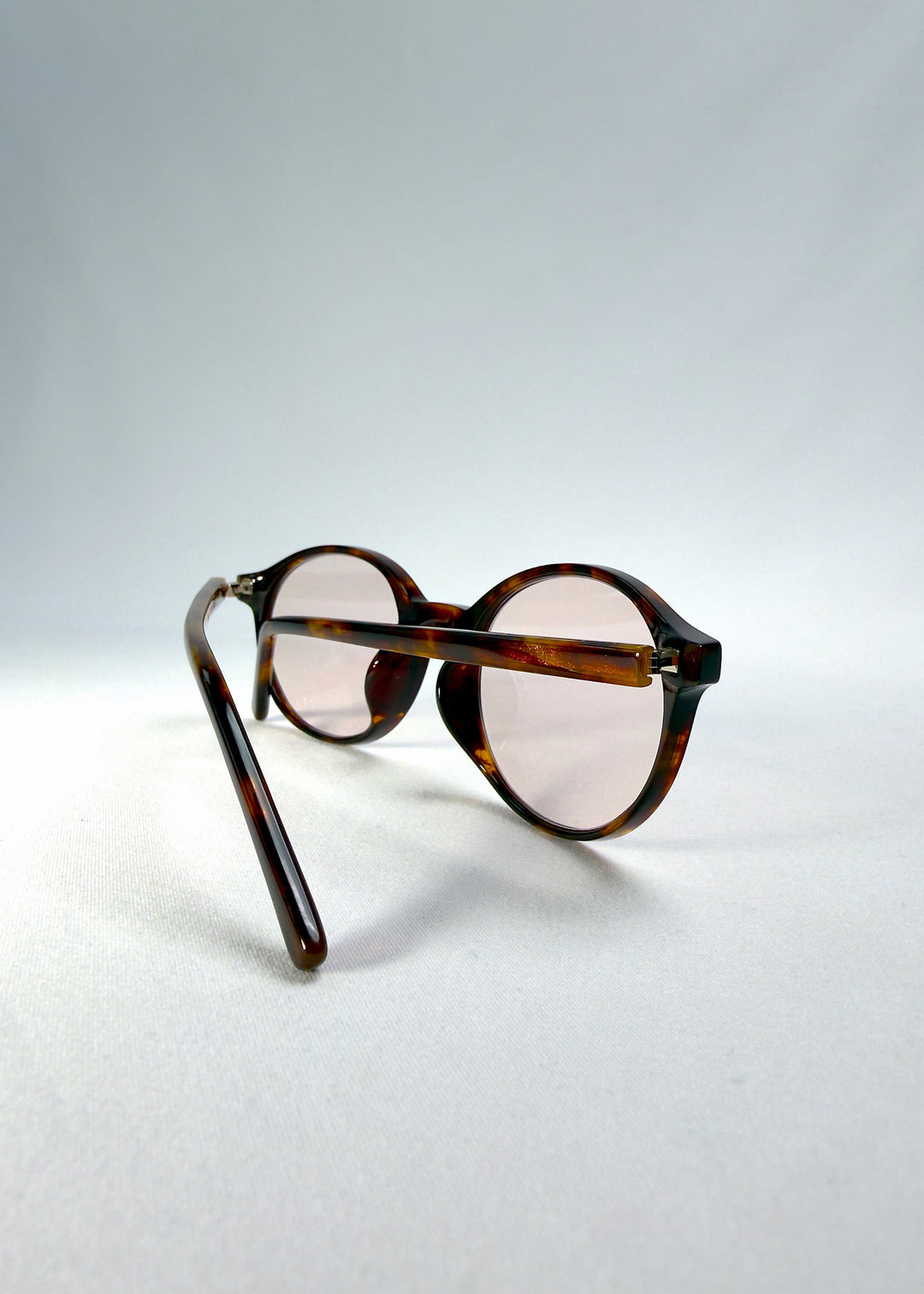Folded-angle view of Glint Softint sunglasses in Umber Ripple featuring amber-brown acetate temples and light pink Softint lenses. 