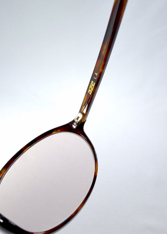 Close-up of Glint Softint sunglasses in Umber Ripple showing AZE logo and amber tortoise acetate texture. 