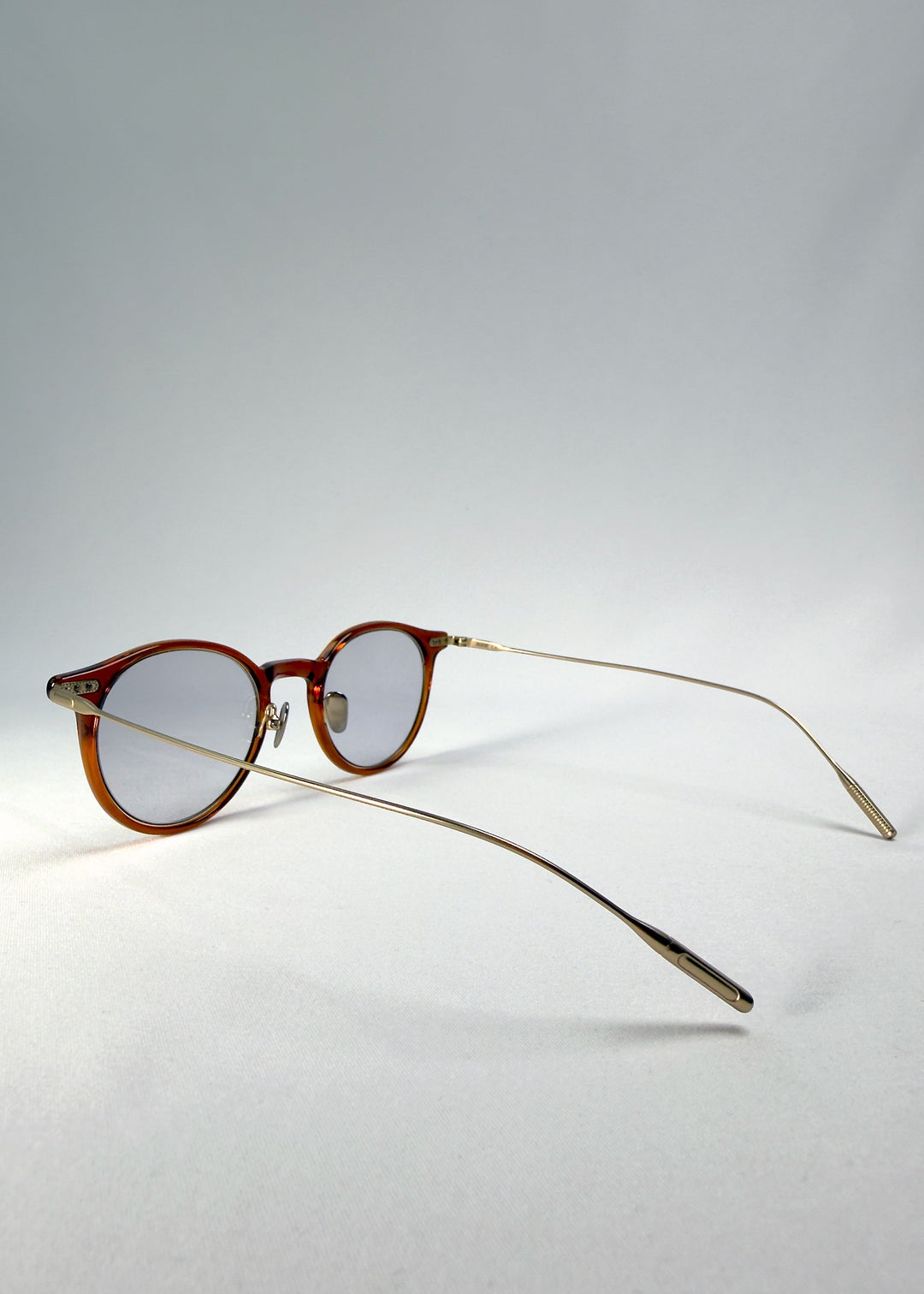 Back-angle view of Lunor Drift Softint sunglasses in Amber Mist displaying slender metal arms and warm amber frame details. 
