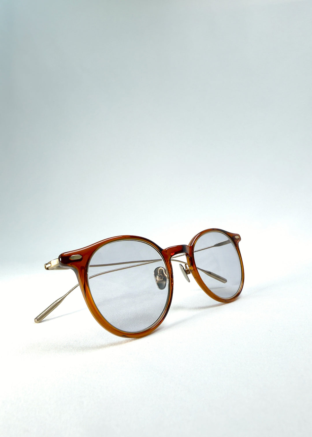 Front-angle view of Lunor Drift Softint sunglasses in Amber Mist featuring translucent amber frame and gold titanium temples.