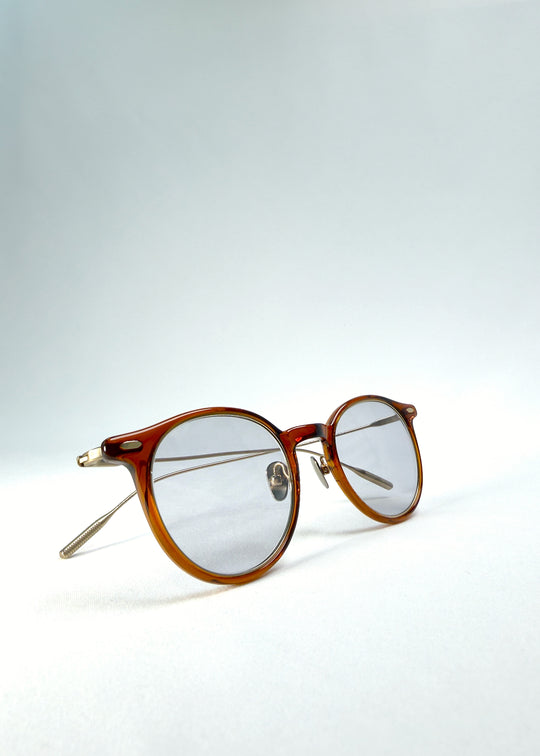 Front-angle view of Lunor Drift Softint sunglasses in Amber Mist featuring translucent amber frame and gold titanium temples.