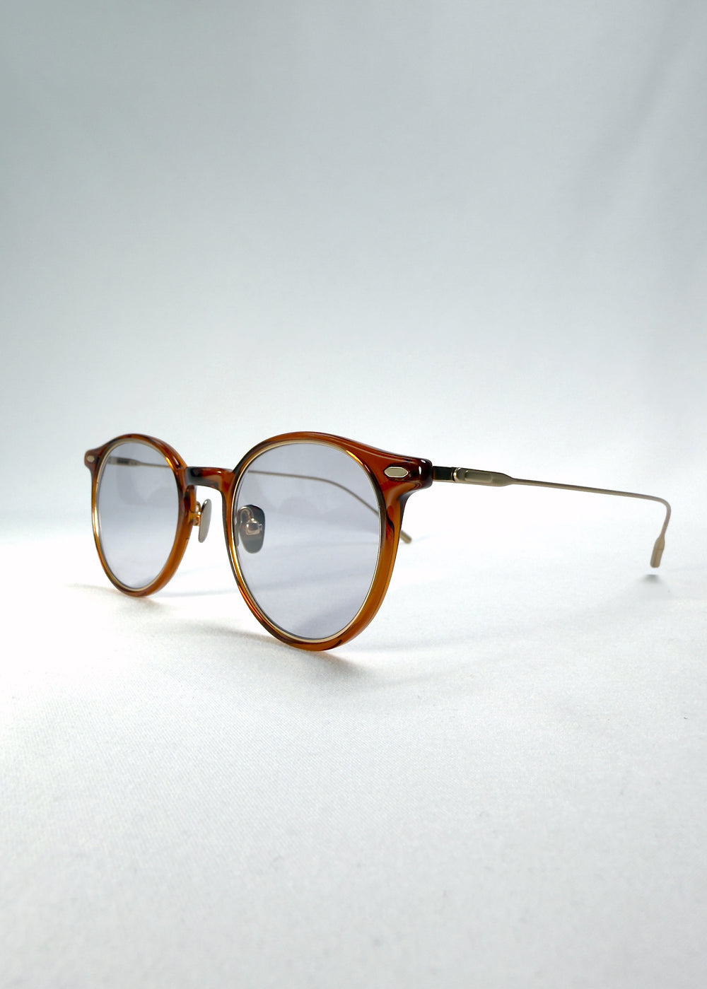 Close-up of Lunor Drift Softint sunglasses in Amber Mist showing lens reflection and gold hinge detail.