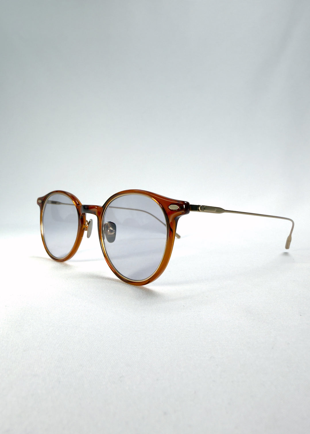 Close-up of Lunor Drift Softint sunglasses in Amber Mist showing lens reflection and gold hinge detail.