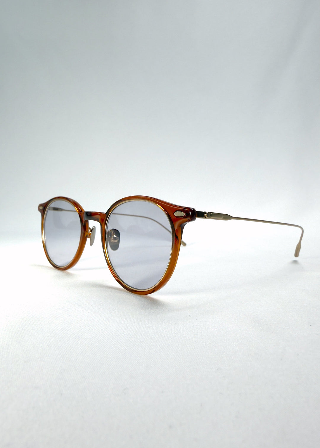 Close-up of Lunor Drift Softint sunglasses in Amber Mist showing lens reflection and gold hinge detail. 