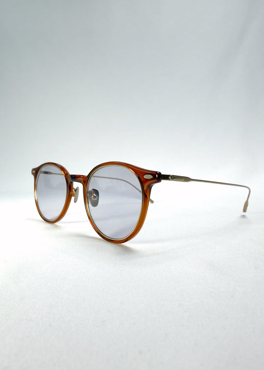 Close-up of Lunor Drift Softint sunglasses in Amber Mist showing lens reflection and gold hinge detail. 