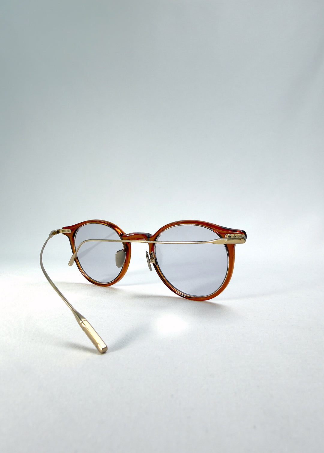 Side-temple view of Lunor Drift Softint sunglasses in Amber Mist showing curved gold titanium temples and amber acetate frame.