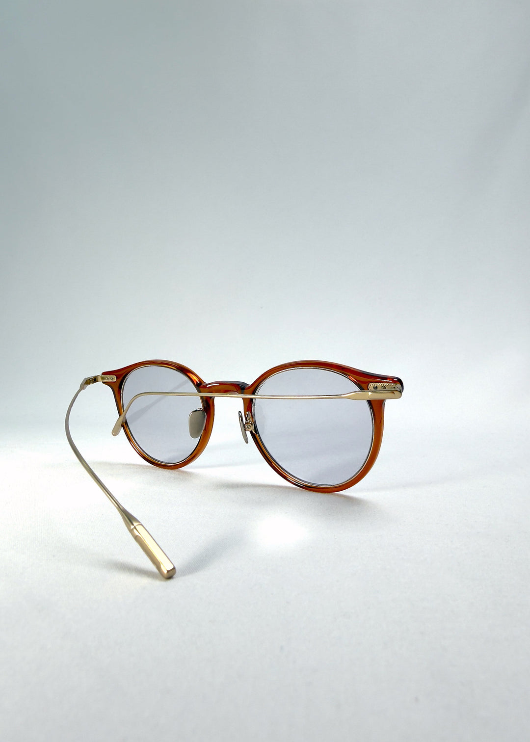 Side-temple view of Lunor Drift Softint sunglasses in Amber Mist showing curved gold titanium temples and amber acetate frame. 