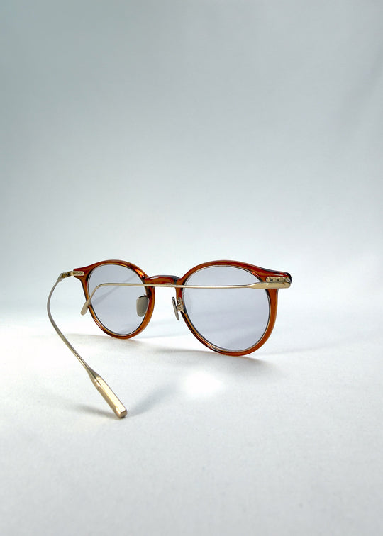Side-temple view of Lunor Drift Softint sunglasses in Amber Mist showing curved gold titanium temples and amber acetate frame. 