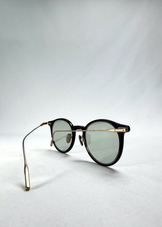 Folded-angle view of Lunor Drift Softint sunglasses in Shadow Gleam featuring slim gold titanium arms and acetate front frame. 