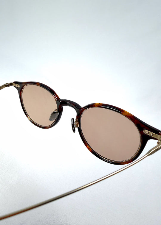 Close-up of Lunor Drift Softint sunglasses in Umber Fade showing gold hinge detail and warm amber acetate frame texture. 