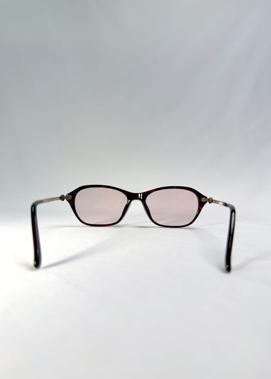 Back-angle view of Ravynor Softint sunglasses in Burnt Amber showing silver-metal temples and warm amber frame. 