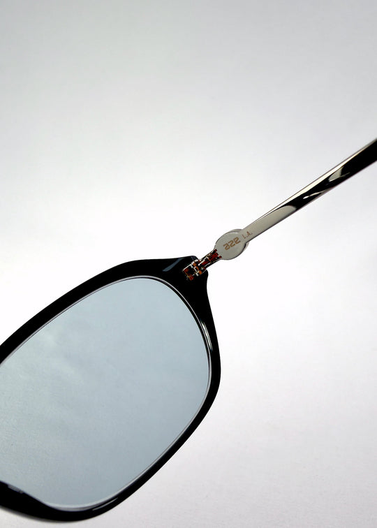 Close-up of Ravynor Softint sunglasses in Noir Alloy showing lens tint and silver hinge detail with sleek black frame finish. 
