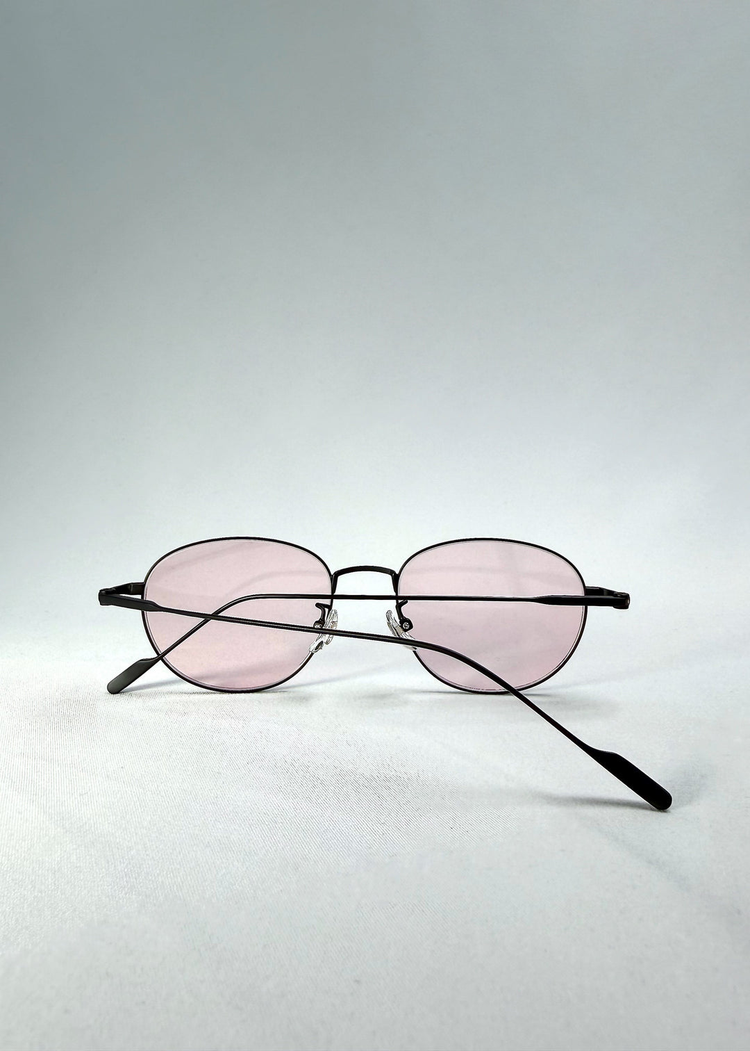 Folded view of Solen Softint sunglasses in Nightveil, showing the slim metal frame and pale rose lenses. 