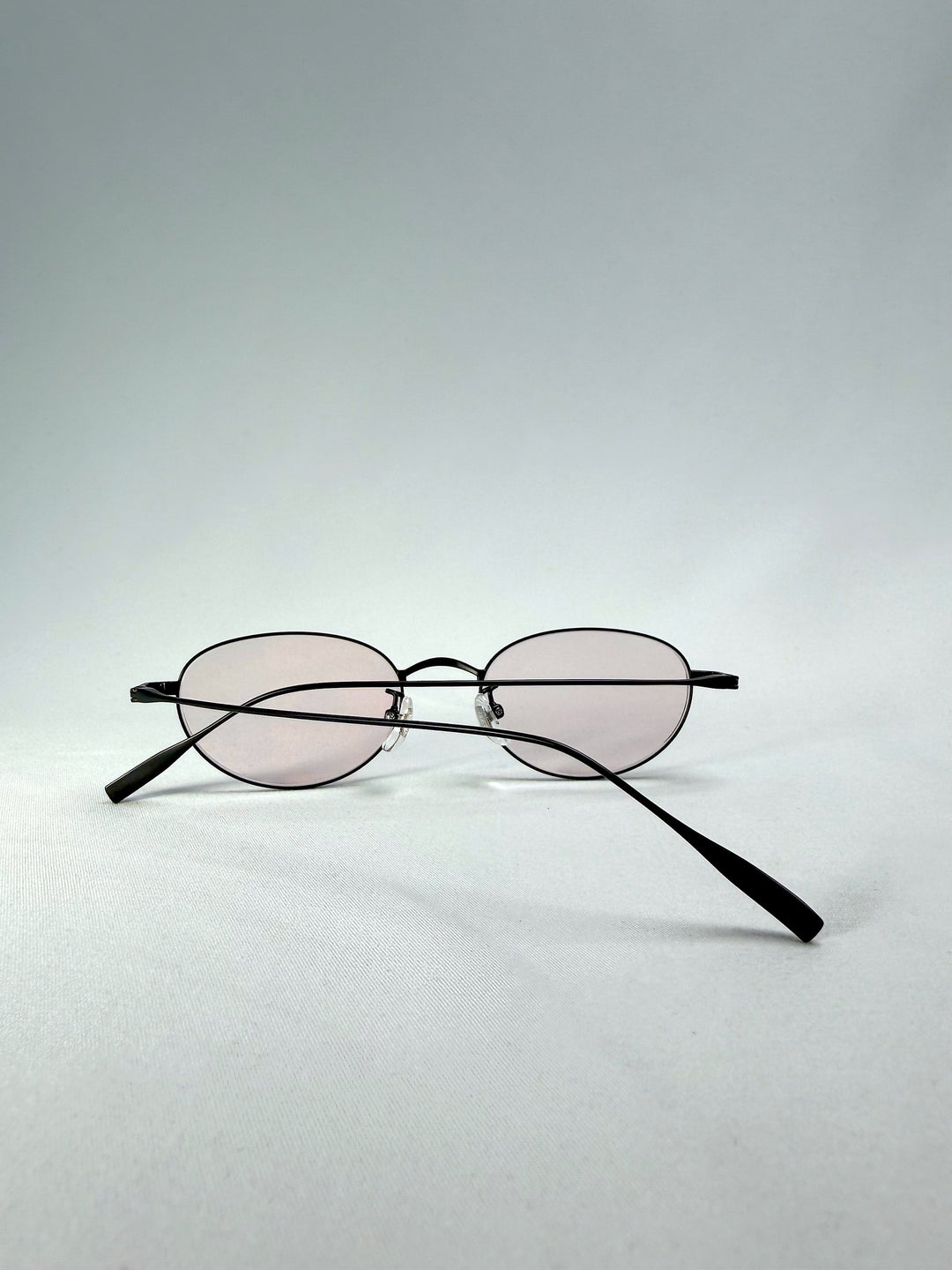 Folded-back view of Vanta Arc Softint sunglasses in Blush Noir showing the matte black frame and pale blush lenses. 