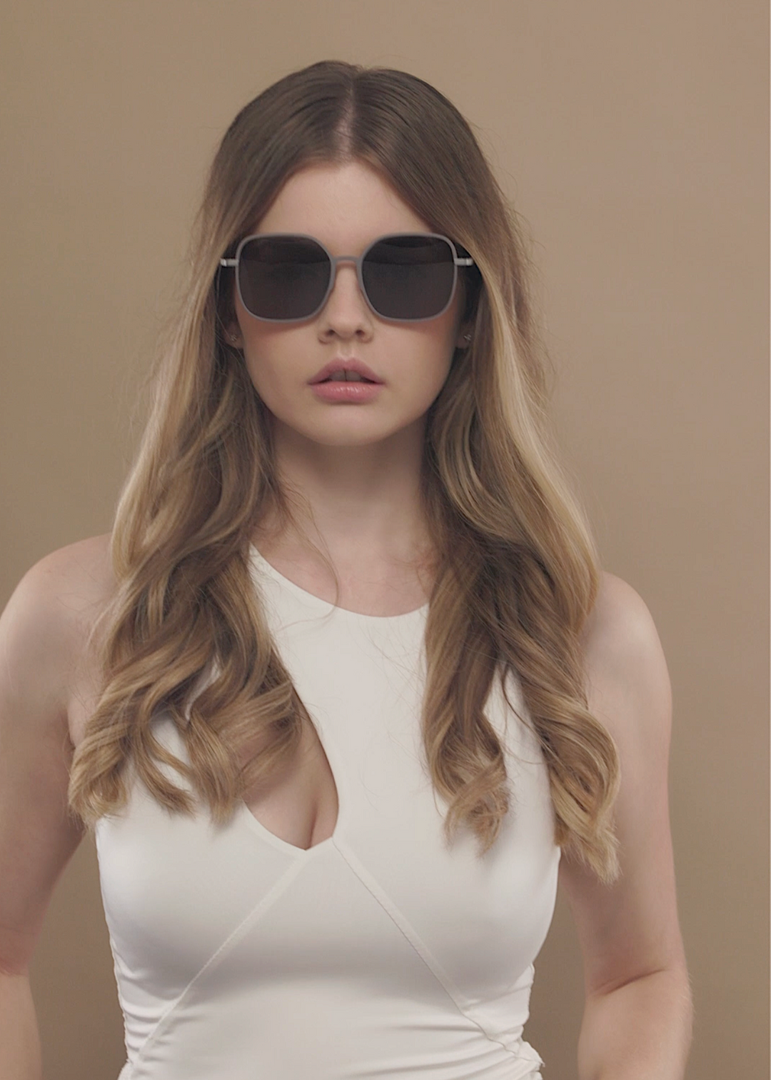 Female model wearing Spica sunglasses in Milk Tea Brown with a white sleeveless top, facing forward. 
