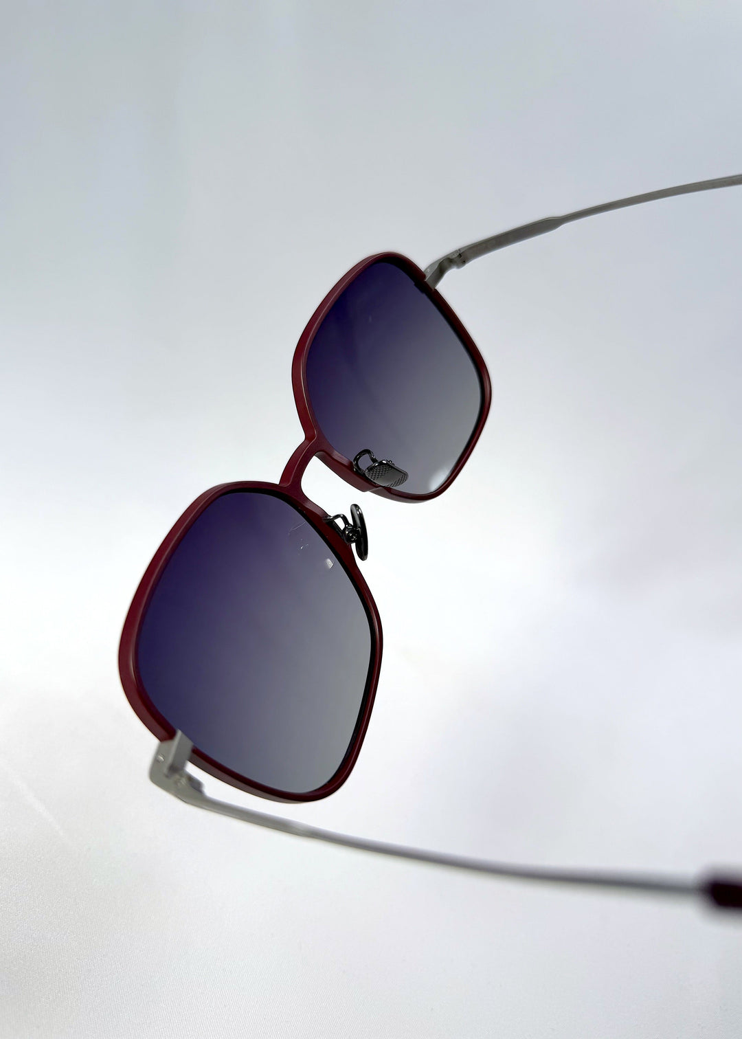 Close-up temple detail view of Spica sunglasses in Cherry Red, featuring an ultra-light frame with titanium temples and polarized lenses, showing the temple arm and hinge area. 