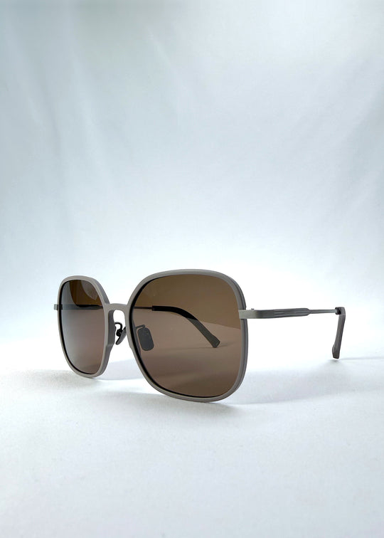 Three-quarter front view of Spica sunglasses in Milk Tea Brown, featuring an ultra-light frame with titanium temples and polarized lenses, showing the front shape and temple profile. 