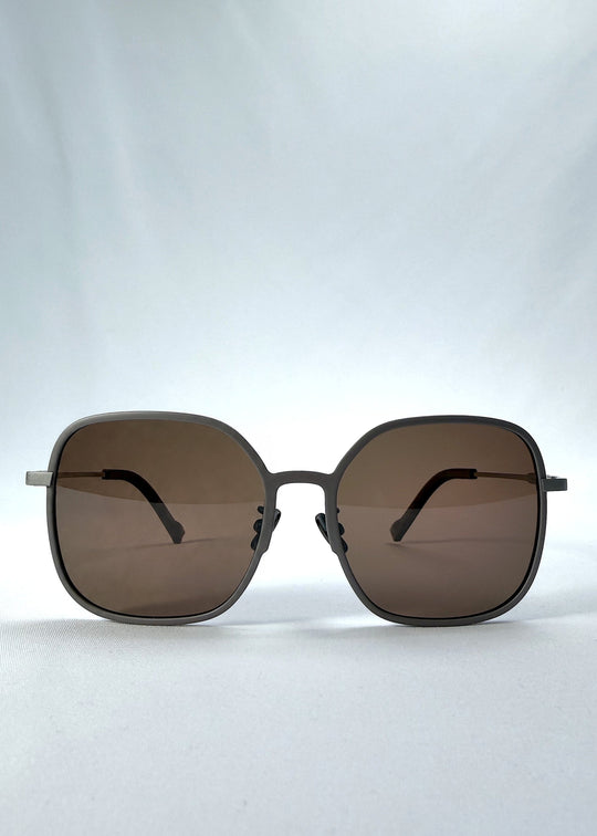 Front view of Spica sunglasses in Milk Tea Brown, featuring an ultra-light frame with titanium temples and polarized lenses, showing the full front silhouette. 