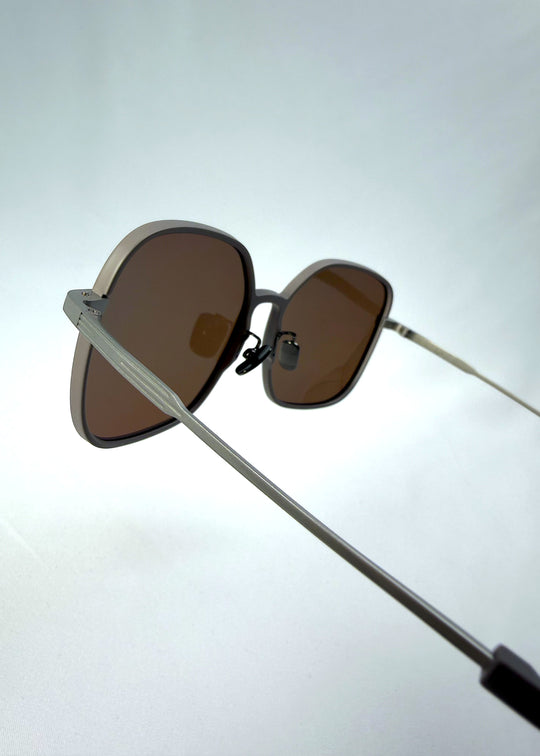 Close-up temple detail view of Spica sunglasses in Milk Tea Brown, featuring light titanium frame and polarized lenses, showing the temple arm and hinge area.