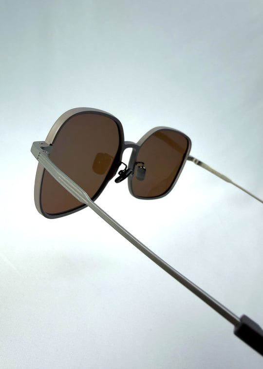 Close-up temple detail view of Spica sunglasses in Milk Tea Brown, featuring an ultra-light frame with titanium temples and polarized lenses, showing the temple arm and hinge area. 