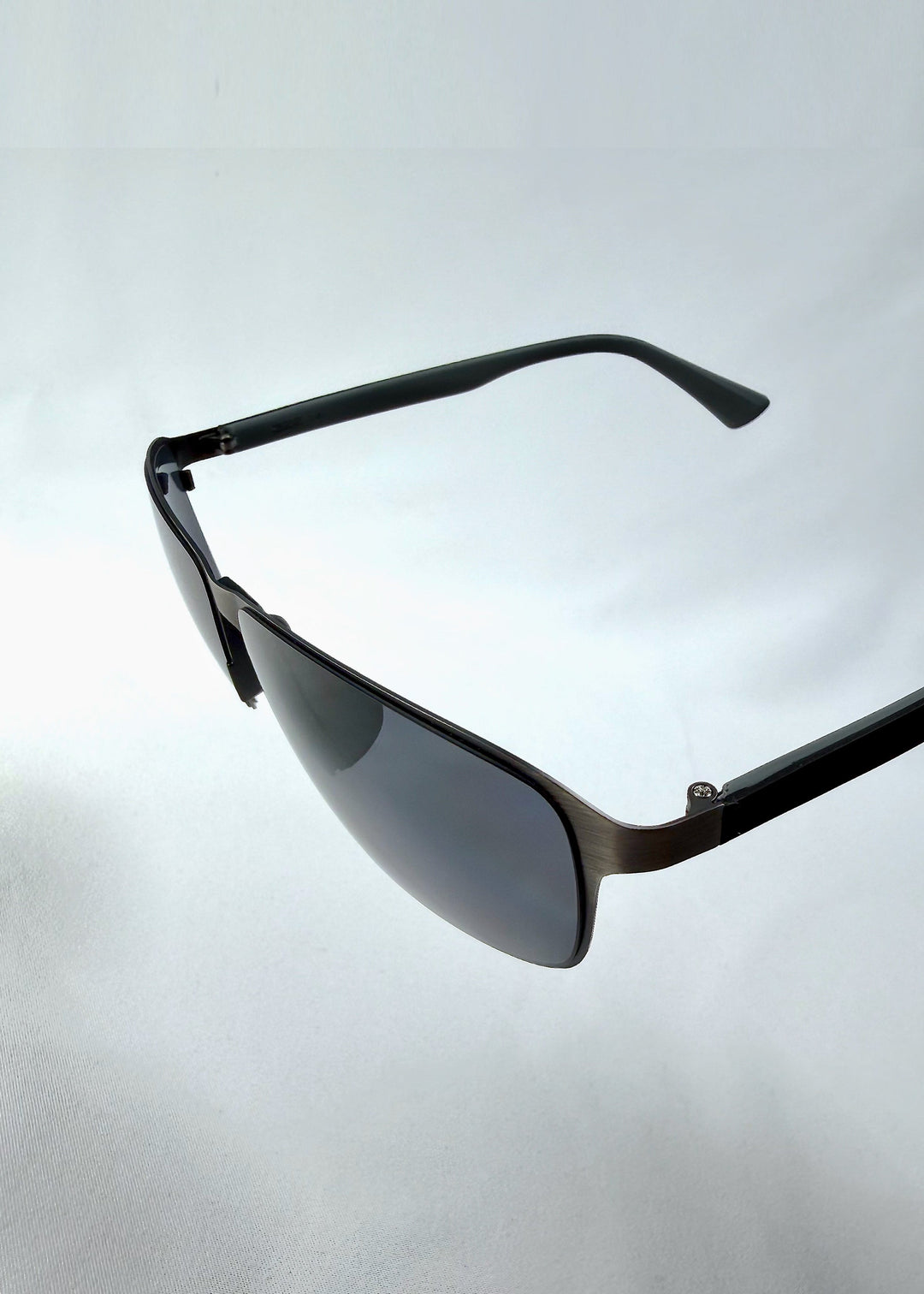 Close-up side detail view of Vector Line sunglasses in Matte Black, featuring wide matte black rectangular metal frame and full grey polarized lenses, showing the lens edge, hinge area, and temple detail. 