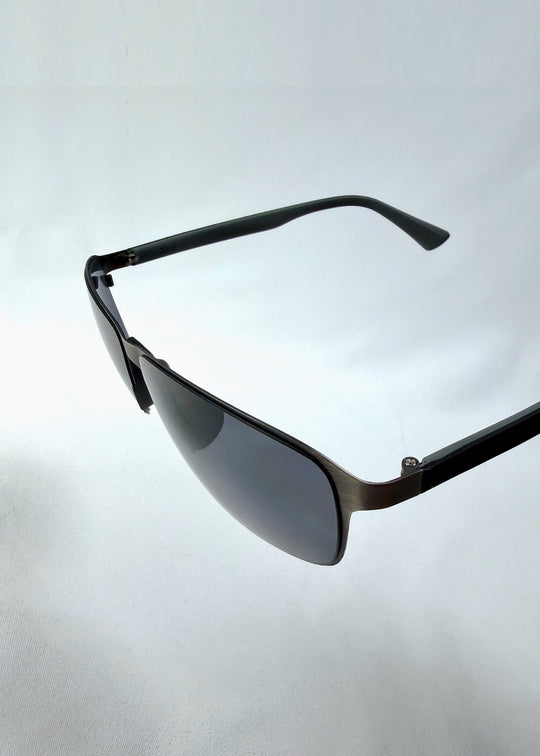 Close-up side detail view of Vector Line sunglasses in Matte Black, featuring wide matte black rectangular metal frame and full grey polarized lenses, showing the lens edge, hinge area, and temple detail. 