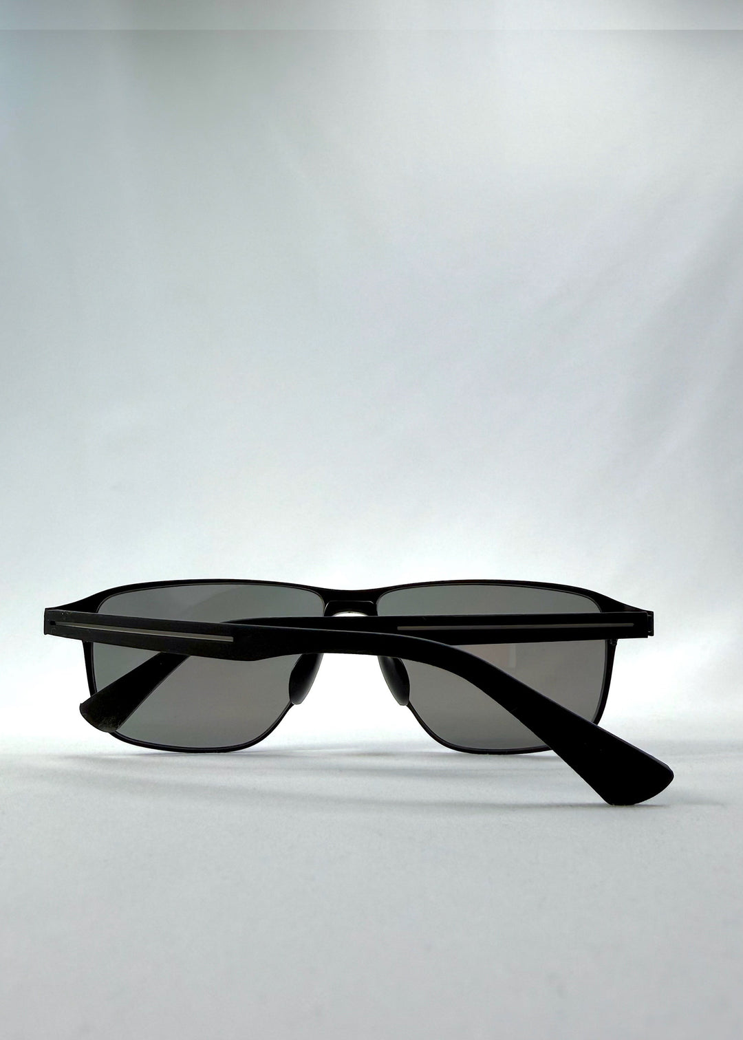 Folded view of Vector Line sunglasses in Mercury Shadow, featuring wide black metal frame and silver mirrored polarized lenses, showing the folded temples and frame profile. 