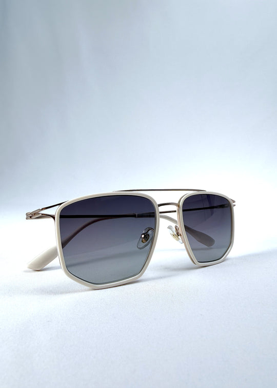 Folded view of AZE Vela Trace sunglasses in Glacial Smoke, featuring a pale gold-tone rectangular frame and blue-gray gradient lenses, showing the folded temples and frame profile.
