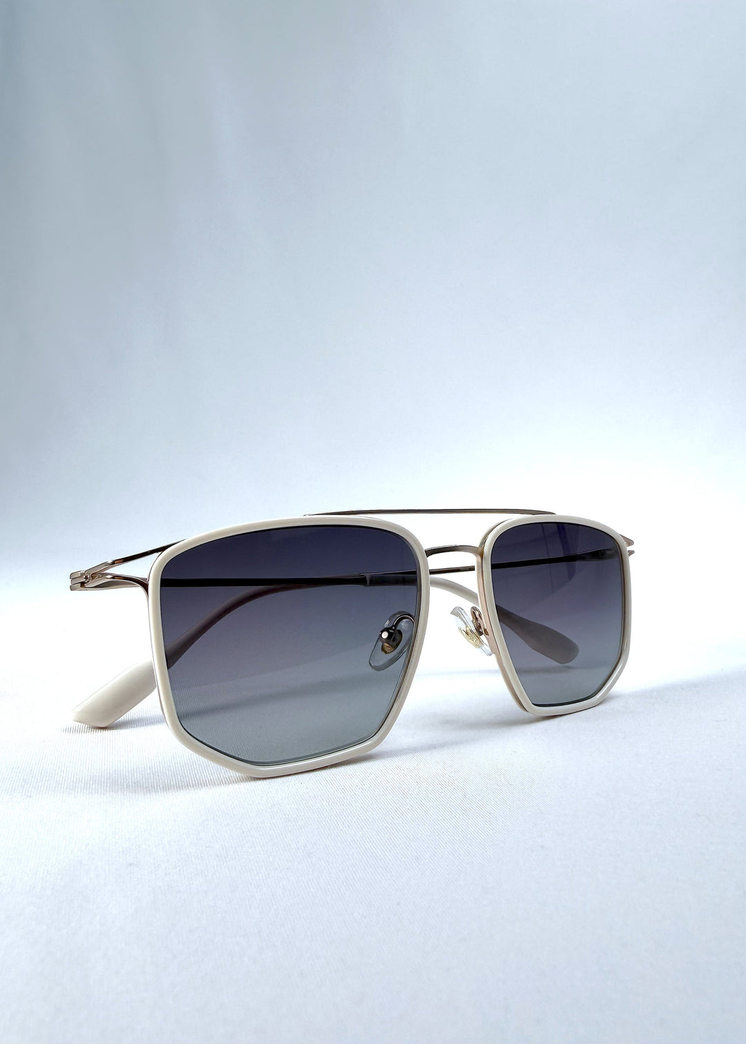 Folded view of AZE Vela Trace sunglasses in Glacial Smoke, featuring a pale gold-tone rectangular frame and blue-gray gradient lenses, showing the folded temples and frame profile. 