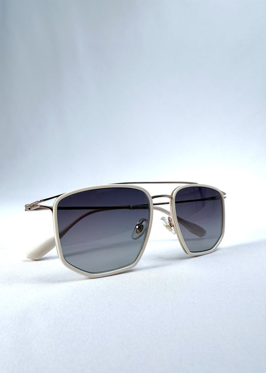 Folded view of AZE Vela Trace sunglasses in Glacial Smoke, featuring a pale gold-tone rectangular frame and blue-gray gradient lenses, showing the folded temples and frame profile. 