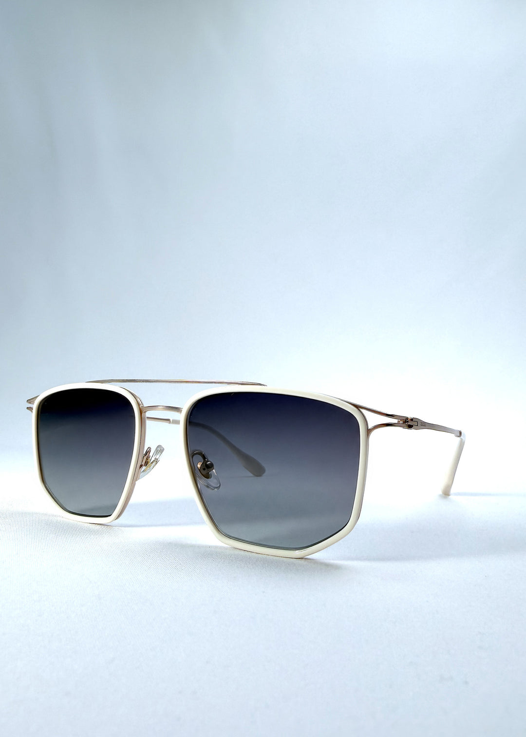 Three-quarter front view of AZE Vela Trace sunglasses in Glacial Smoke, featuring a pale gold-tone rectangular frame and blue-gray gradient lenses, showing the frame shape and temple profile.