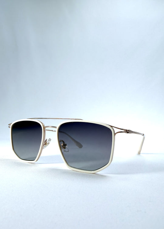 Three-quarter front view of AZE Vela Trace sunglasses in Glacial Smoke, featuring a pale gold-tone rectangular frame and blue-gray gradient lenses, showing the frame shape and temple profile.