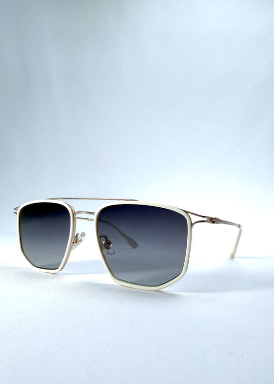 Three-quarter front view of AZE Vela Trace sunglasses in Glacial Smoke, featuring a pale gold-tone rectangular frame and blue-gray gradient lenses, showing the frame shape and temple profile. 