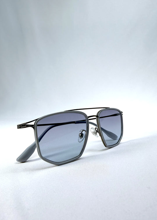 Folded view of AZE Vela Trace sunglasses in Midnight Blue, featuring a gray-blue rectangular frame and blue-gray gradient lenses, showing the folded temples and frame profile.