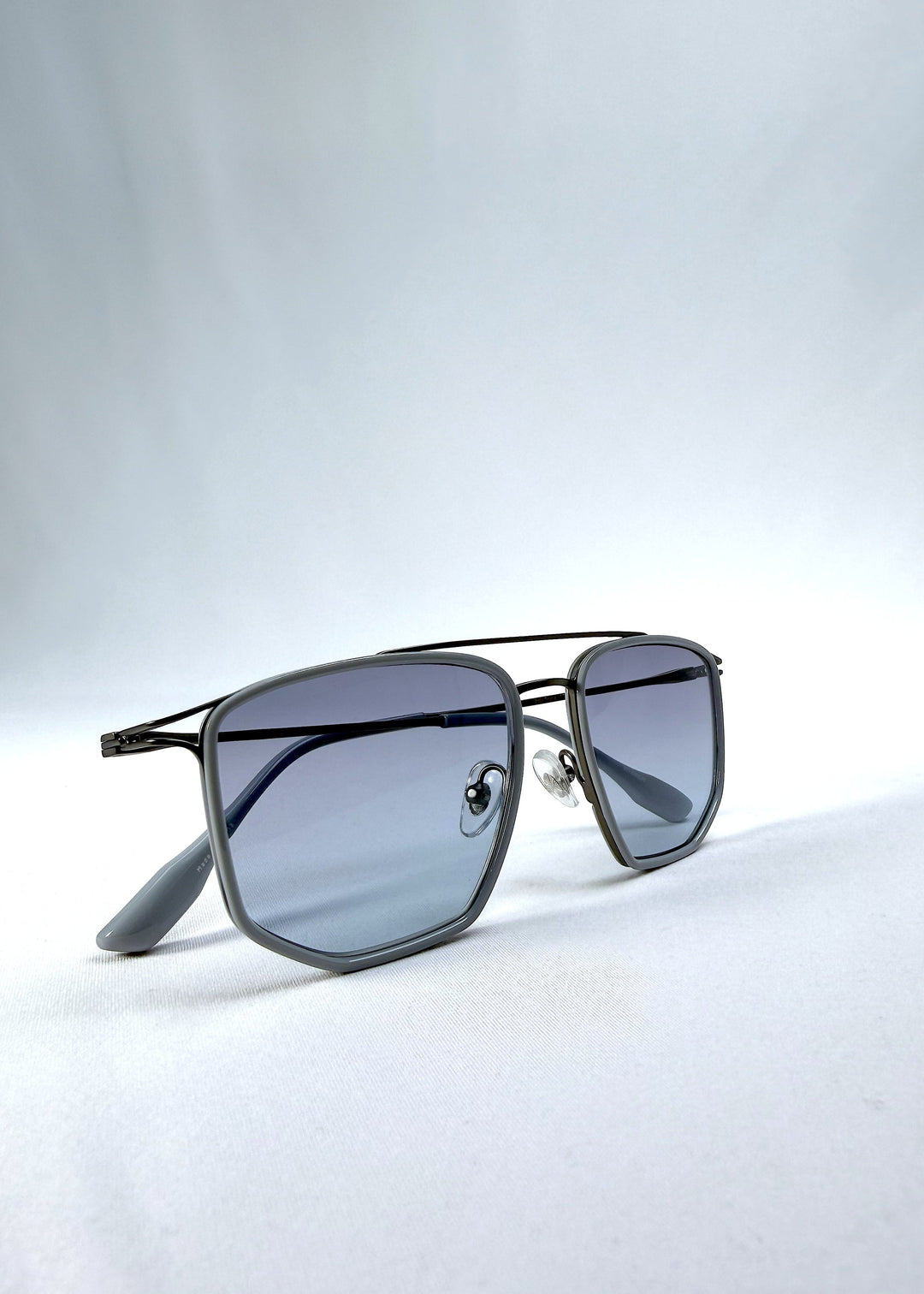 Folded view of AZE Vela Trace sunglasses in Midnight Blue, featuring a gray-blue rectangular frame and blue-gray gradient lenses, showing the folded temples and frame profile. 