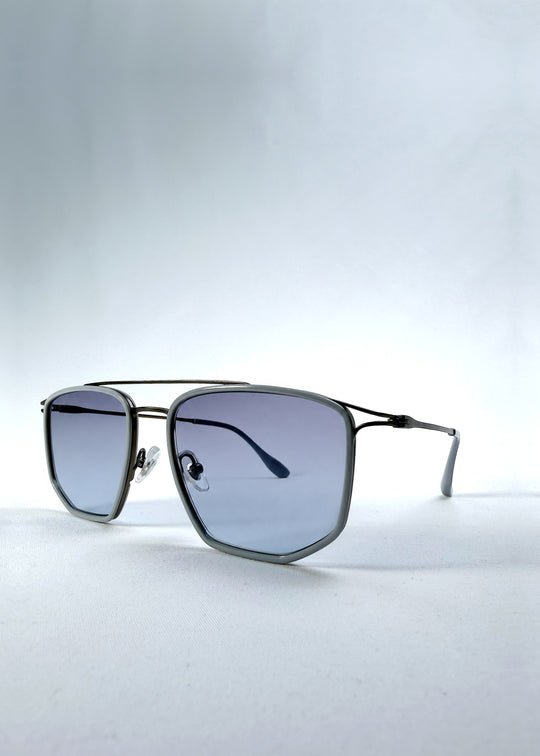 Three-quarter front view of AZE Vela Trace sunglasses in Midnight Blue, featuring a gray-blue rectangular frame and blue-gray gradient lenses, showing the frame shape and temple profile.