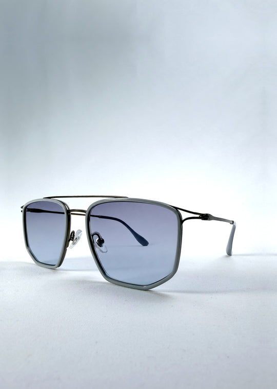 Three-quarter front view of AZE Vela Trace sunglasses in Midnight Blue, featuring a gray-blue rectangular frame and blue-gray gradient lenses, showing the frame shape and temple profile. 