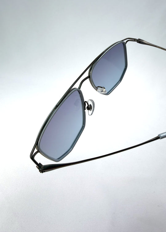 Close-up hinge detail view of AZE Vela Trace sunglasses in Midnight Blue, featuring a gray-blue rectangular frame and blue-gray gradient lenses, showing the hinge construction, lens edge, and temple connection.
