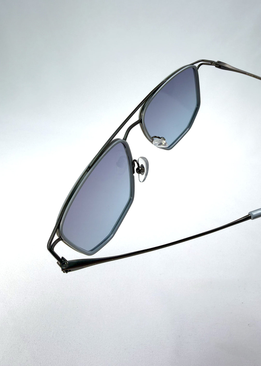 Close-up hinge detail view of AZE Vela Trace sunglasses in Midnight Blue, featuring a gray-blue rectangular frame and blue-gray gradient lenses, showing the hinge construction, lens edge, and temple connection. 