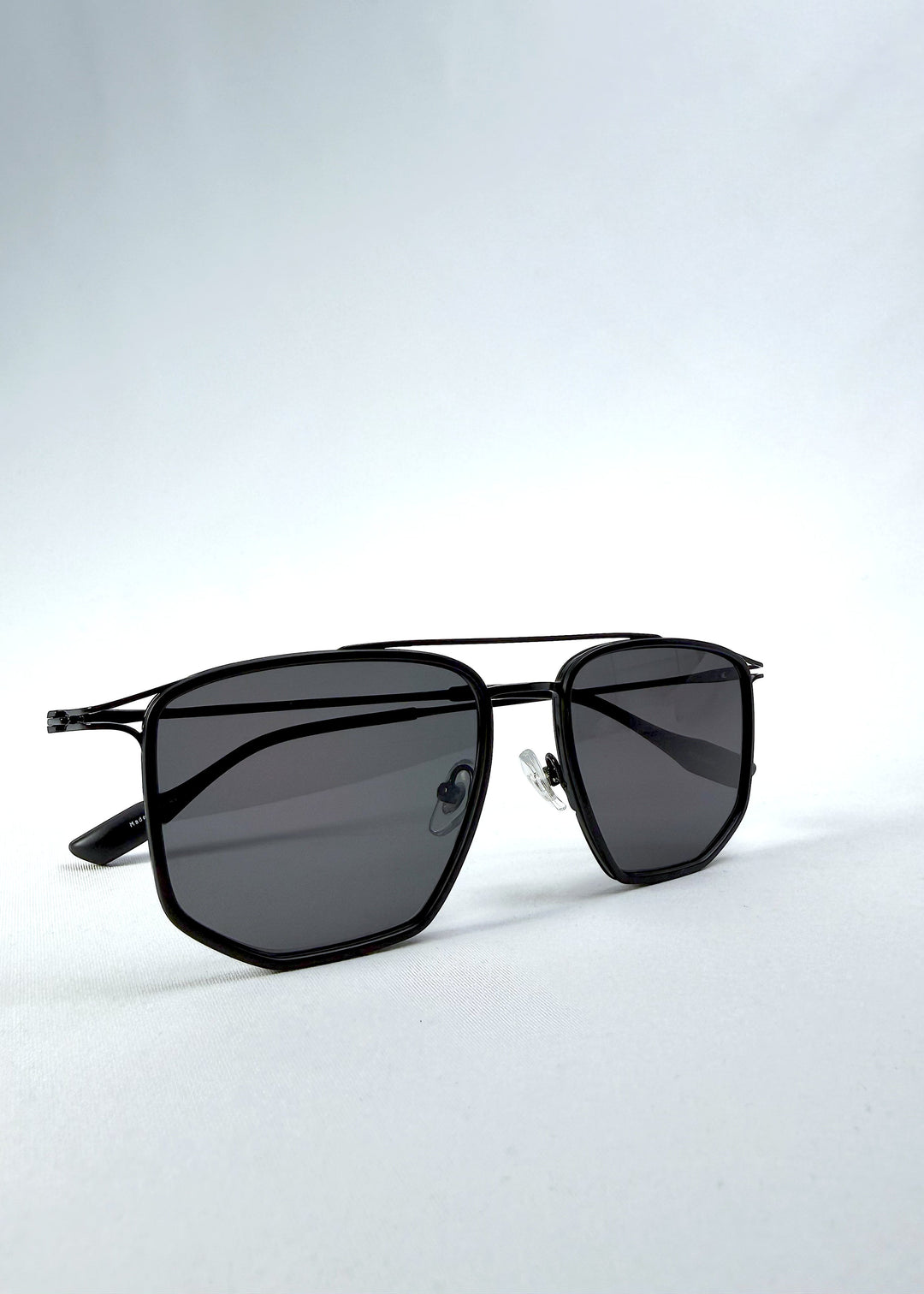 Folded view of AZE Vela Trace sunglasses in Obsidian Black, featuring a structured black rectangular frame and smoky gray lenses, showing the folded temples and frame profile. 
