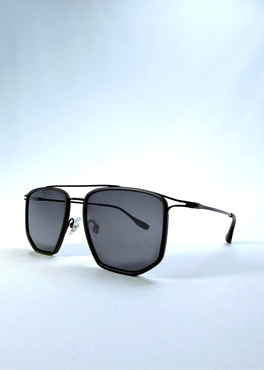 Three-quarter front view of AZE Vela Trace sunglasses in Obsidian Black, featuring a structured black rectangular frame and smoky gray lenses, showing the frame shape and temple profile.