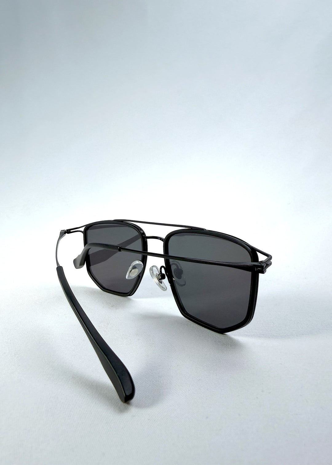 Inside-angle view of AZE Vela Trace sunglasses in Obsidian Black, featuring a structured black rectangular frame and smoky gray lenses, showing the inner frame, nose pads, and temple structure. 