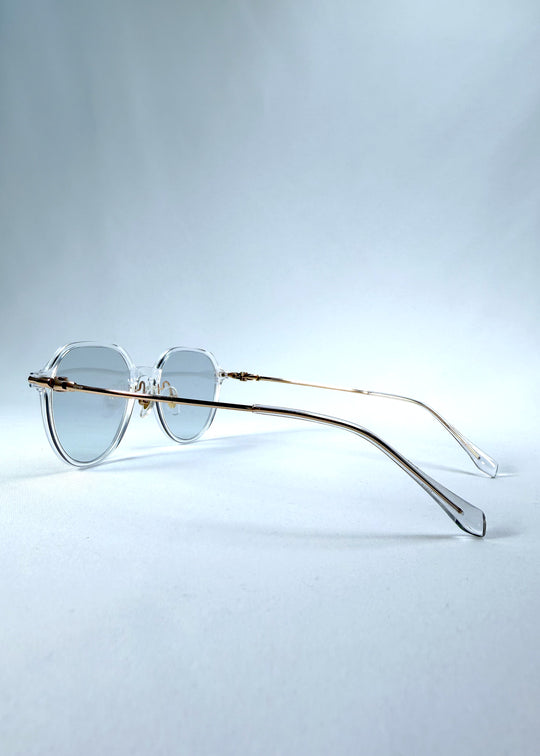 Back-angle view of AZE Vireo Arc sunglasses in Crystal Static, featuring a crystal-clear frame, pale blue lenses, and gold-tone accents, showing the rear frame structure and temple alignment.