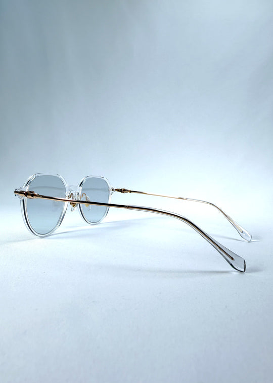 Back-angle view of AZE Vireo Arc sunglasses in Crystal Static, featuring a crystal-clear frame, pale blue lenses, and gold-tone accents, showing the rear frame structure and temple alignment. 