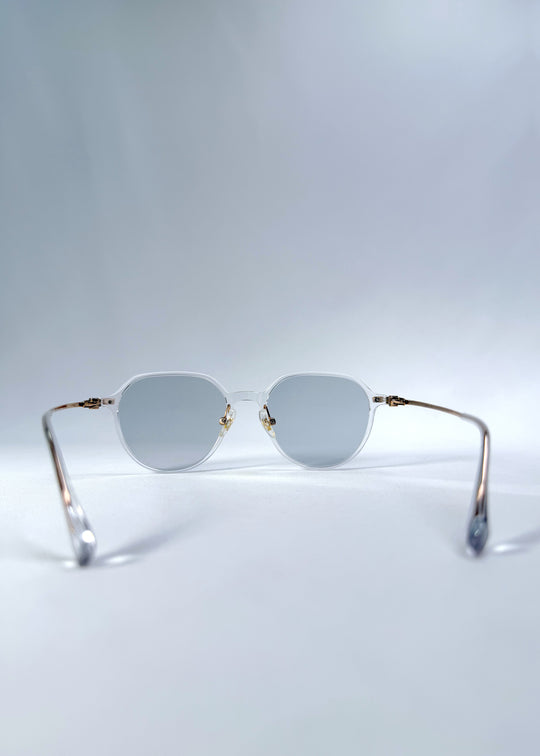 Back view of AZE Vireo Arc sunglasses in Crystal Static, featuring a crystal-clear frame, pale blue lenses, and gold-tone accents, showing the inner frame and open temples.