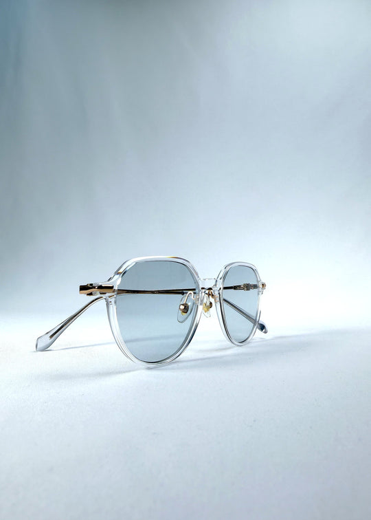 Folded view of AZE Vireo Arc sunglasses in Crystal Static, featuring a crystal-clear frame, pale blue lenses, and gold-tone accents, showing the folded temples and frame profile. 
