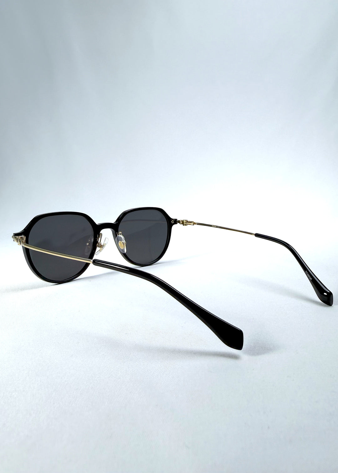 Back-angle view of AZE Vireo Arc sunglasses in Duskgold, featuring a dark softly geometric frame, gold-tone accents, and smoky gray lenses, showing the rear frame structure and temple alignment.