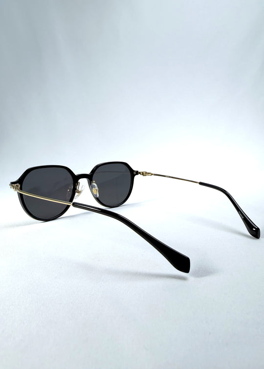 Back-angle view of AZE Vireo Arc sunglasses in Duskgold, featuring a dark softly geometric frame, gold-tone accents, and smoky gray lenses, showing the rear frame structure and temple alignment.