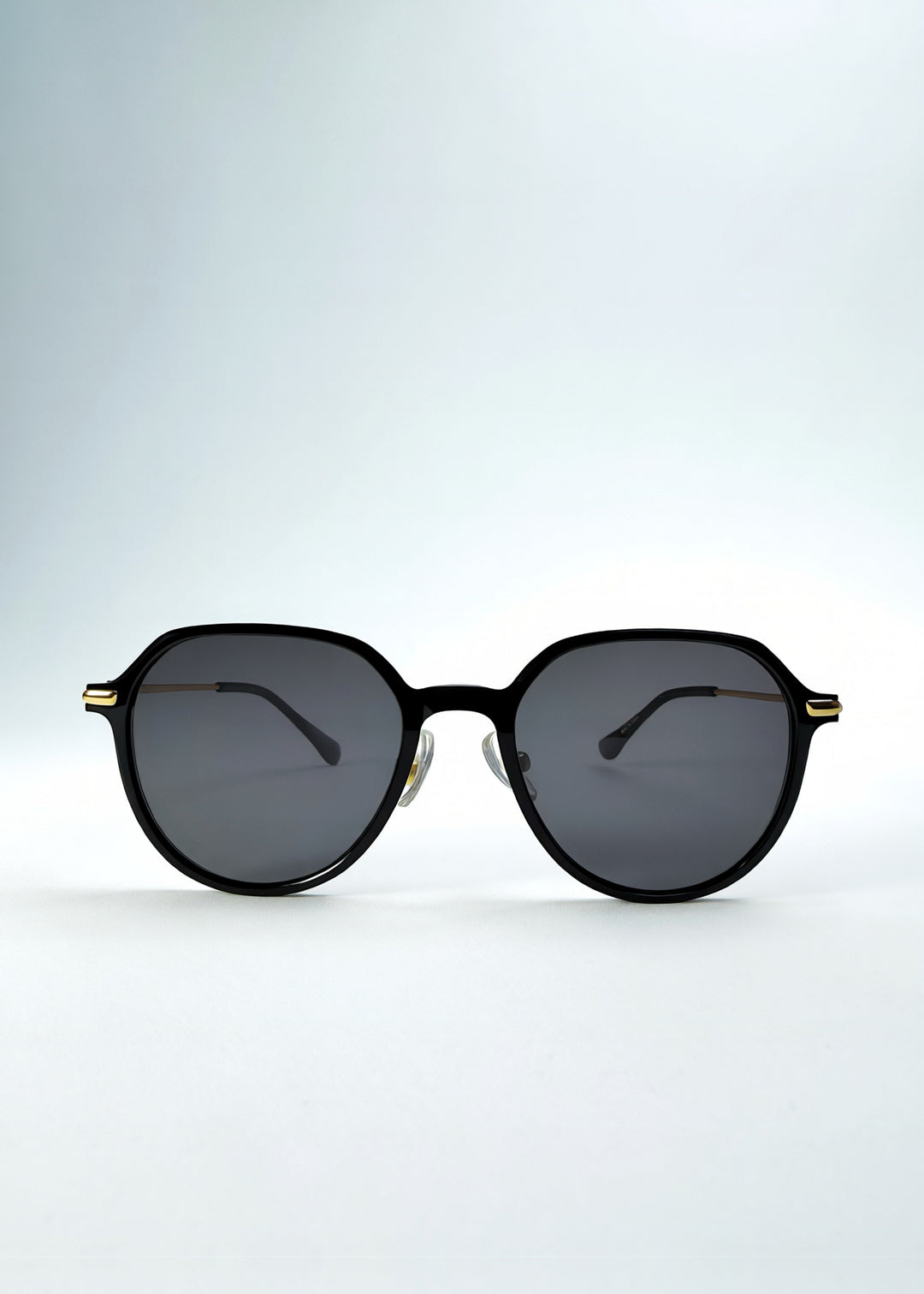 Front view of AZE Vireo Arc sunglasses in Duskgold, featuring a dark softly geometric frame, gold-tone accents, and smoky gray lenses, showing the full front silhouette.