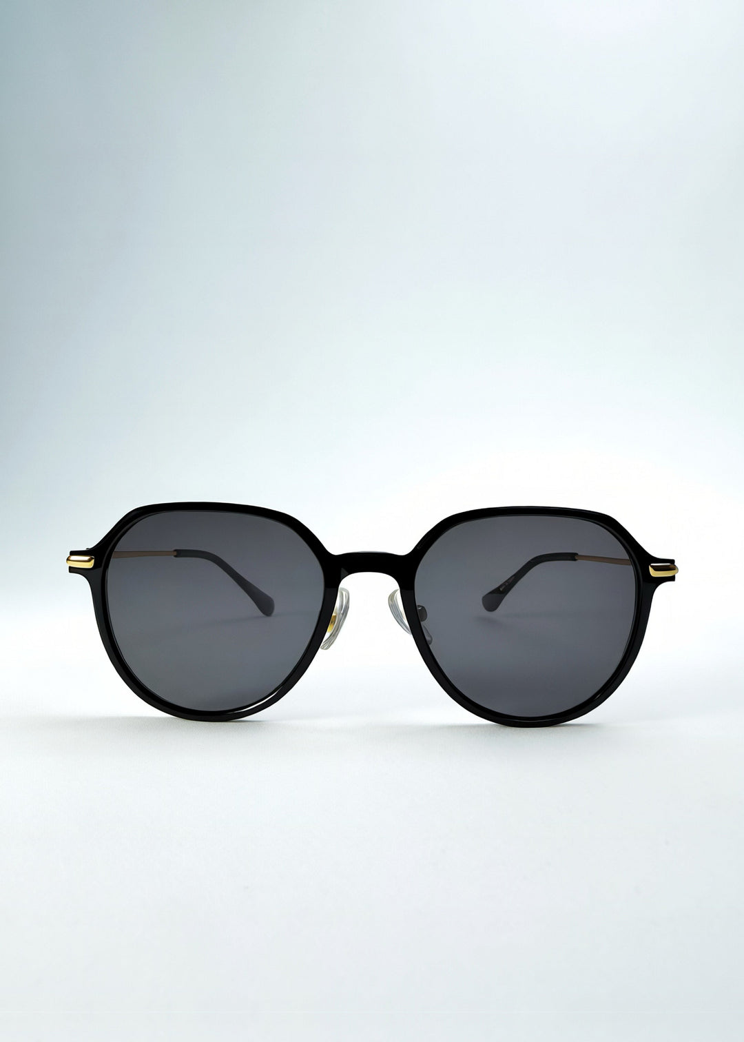 Front view of AZE Vireo Arc sunglasses in Duskgold, featuring a dark softly geometric frame, gold-tone accents, and smoky gray lenses, showing the full front silhouette. 